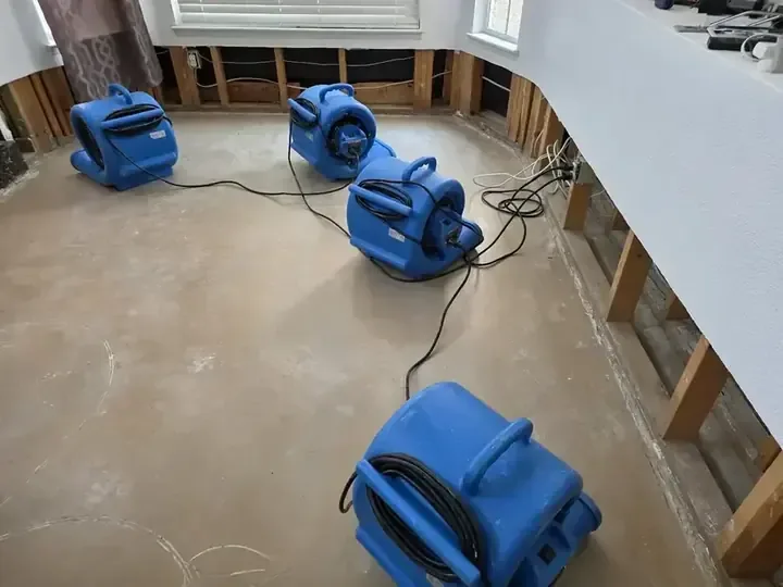 Air movers and a dehumidifier set up in a room during a dry-out