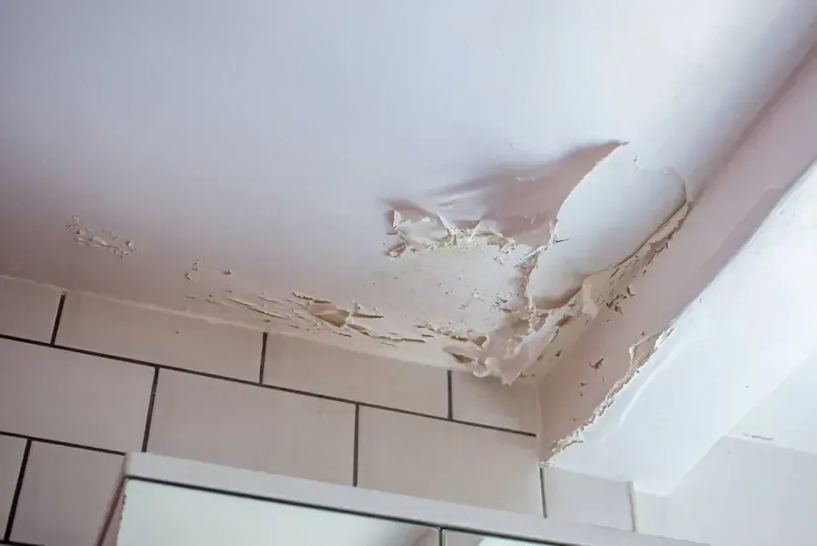 Peeling, water-stained ceiling drywall in a bathroom below a leak